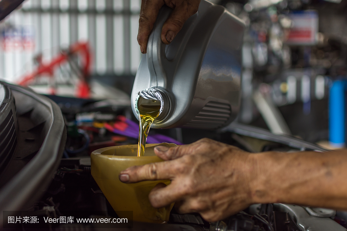 汽车修理工在汽车修理厂为维护一辆汽车注入新鲜的润滑油机油